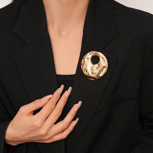 Close-up of a gold hammered metal brooch with abstract round cutout on a black blazer