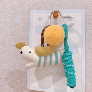 Detail of fabric puppy keychain with yellow pompom and blue braided rope on metal clip