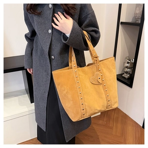 Model wearing a yellow suede tote bag with rivets and heart pendant in a stylish setting