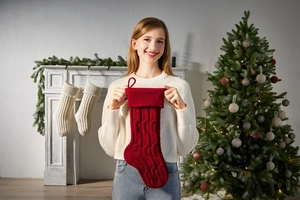 Cozy knit Christmas stocking in red being held in front of a festive fireplace