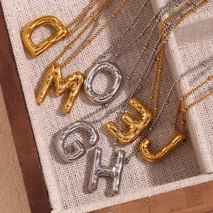 Detail van 18K goud en zilveren ballonletter hangers in een houten sieradendoosje