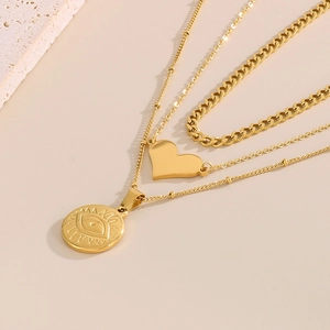 Dettaglio della collana dorata a strati con ciondolo a cuore e medaglione occhio