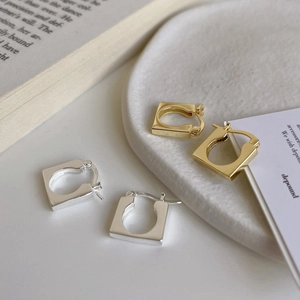 Pair of gold and silver S925 sterling silver square hoop earrings on a minimalist tray