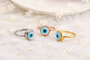 Detailed macro view of gold, silver, and rose gold evil eye rings on white lace fabric