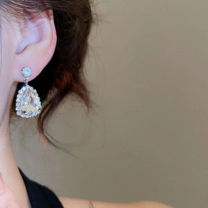 Detail view of teardrop crystal earrings with silver finish worn by a model in soft light