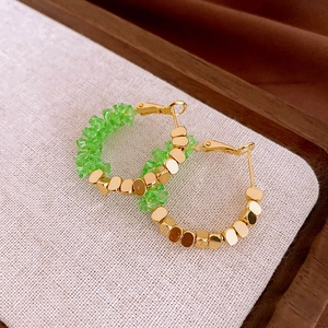 Detailed close-up of golden wheat ear earrings with green crystal beads on a linen tray