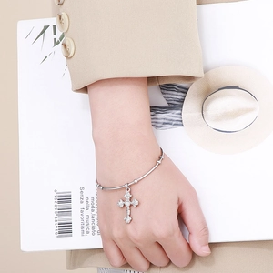 Close-up of a silver cross charm bracelet with heart and petal motifs on a female wrist