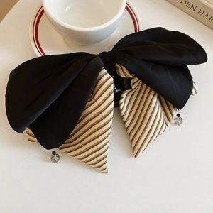 Détail d'une pince à cheveux avec nœud contrasté, tissu rayé et breloques cristal