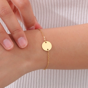 Close-up of minimalist gold circular pendant bracelet on model with white knit fabric