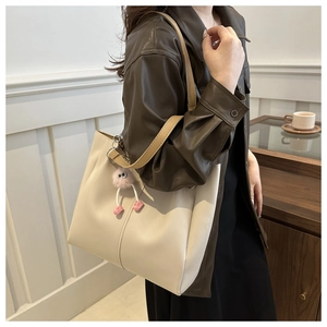 Elegante borsa tote beige con spalline marroni e ciondolo di peluche sulla spalla