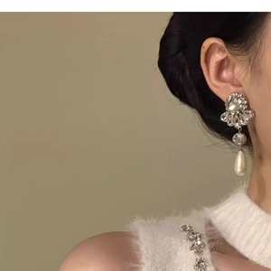 Close-up of a floral rhinestone earring with a teardrop pearl pendant on a model