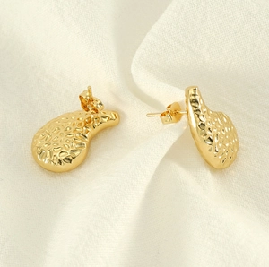 Détail macro de boucles d'oreilles goutte dorées avec texture martelée et design organique