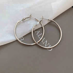 Detailed view of silver hoop earrings with pin closure on white silk fabric background