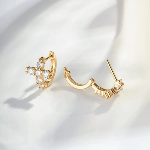 Elegant gold cross earrings with clear zircon stones on soft cream fabric background