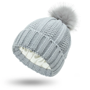 Detail of gray knit beanie showing the protective white satin lining and soft faux fur pom
