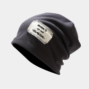 Detail of dark grey knit beanie featuring a white frayed patch and black embroidery