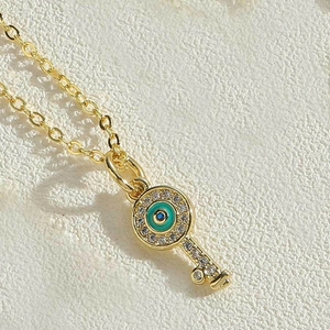 Macro shot of gold key pendant necklace featuring evil eye charm and crystal pave details