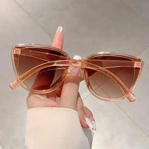 Detail of amber cat eye sunglasses with brown gradient lenses held by a model