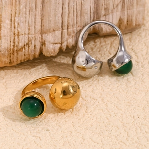 Detail of 18K gold and silver open rings with green agate stones on sand surface
