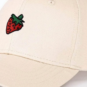 Detailed close-up of red strawberry embroidery on beige cotton twill baseball cap