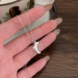 Minimalist S925 sterling silver croissant pendant necklace held over a rustic cafe table
