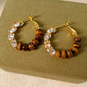 Detail of gold hoop earring with tiger eye stone and zircon on green velvet box
