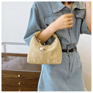 Détail d'un sac plissé beige avec accessoire à perles porté sur une jupe en jean