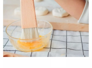 Détail d'un pinceau à pâtisserie en bois appliquant de la dorure sur la pâte