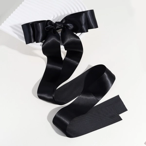 Detailed close-up of a glossy black satin ribbon bow clip with long streamers on white wave