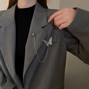 Detailed view of silver butterfly brooch with hammer texture on lapel of grey blazer