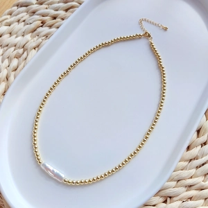 Detail of bohemian gold beaded necklace with a natural white baroque pearl on a ceramic tray