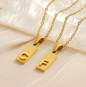 Detail of square gold pendants with frosted metal texture featuring letters C and F