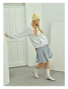 Full body view of a grey hoodie, blue pleated skirt and yellow knitted beanie outfit