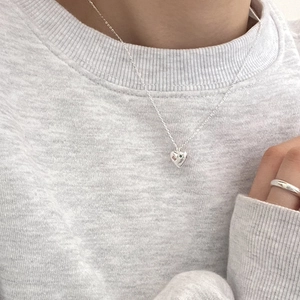 Close-up of minimalist silver heart necklace with a tiny gemstone on a gray sweater