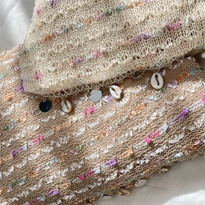 Detail of beige crochet tote bag with colorful yarns, sequins, and natural shells