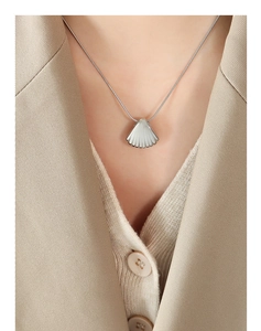 Close-up of a silver-tone seashell pendant necklace worn by a model in a beige suit