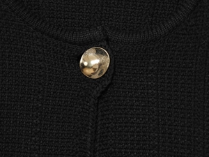 Detailed close-up of textured black knit fabric featuring a hammered gold metal button