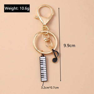 Detail view of a gold musical keychain with piano key and black note charms, 9.9cm length