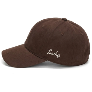Detail of white Lucky embroidery on the side of a premium dark brown cotton baseball cap