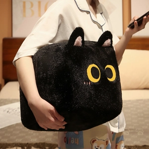 Detail of a large black plush square cat pillow with yellow eyes held by a model