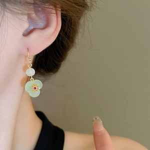 Detailed close-up of jade-like flower earrings with gold hooks on a person