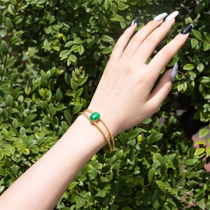 Detail of twisted gold rope cuff featuring a large oval green gemstone on a model's wrist