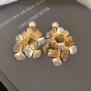 Detailed close-up of golden layered flower petal earrings with a white pearl accent