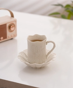 Detailed macro view of the cream ceramic tea cup with embossed floral patterns and bamboo handle