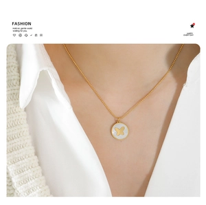 Close-up of a gold butterfly necklace with shell pendant worn by a model in a shirt