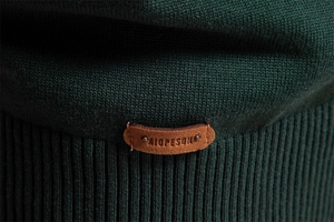 Close-up of dark green ribbed knit texture with a premium brown leather logo patch