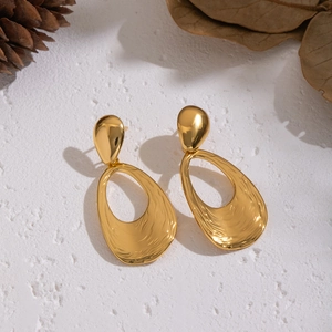 Detail of gold water ripple textured teardrop earrings on a white textured background