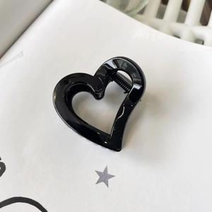 Close-up of black glossy heart-shaped hair claw clip with cutout design on white book