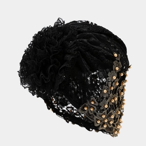Détail du turban en dentelle noire avec fleur plissée et bordure en perles dorées