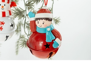 Close-up of red metal star cutout bell with painted doll hanging on pine branch